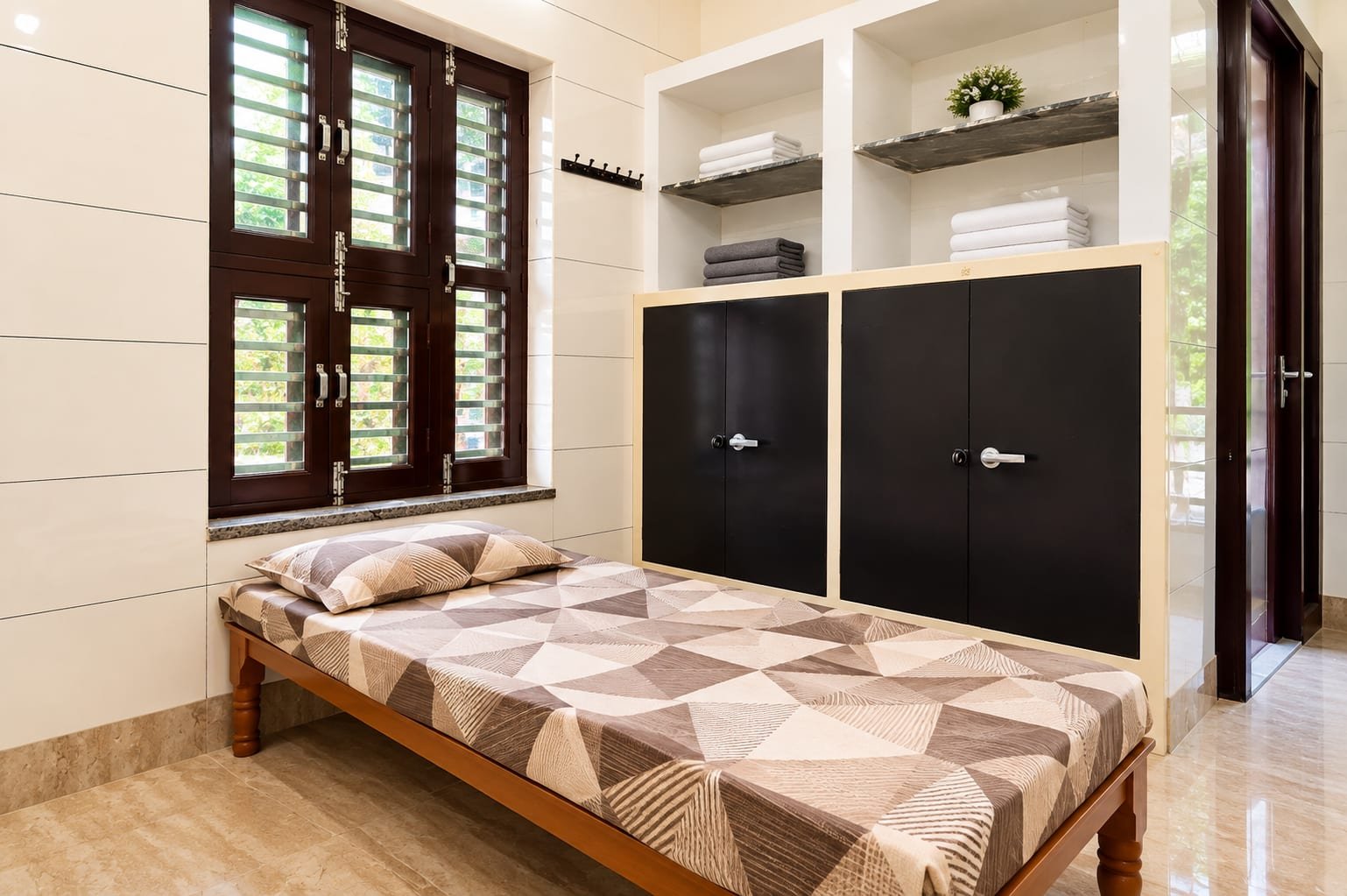 A single room with the bed beside the window, two lockers and open shelves for towels